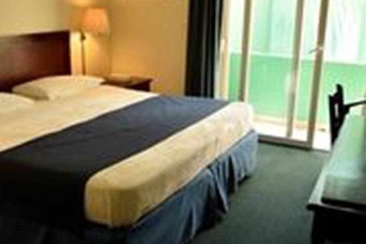Ein Hotelzimmer mit einem großen Bett, einem Nachttisch, einer Lampe und Blick ins Freie.