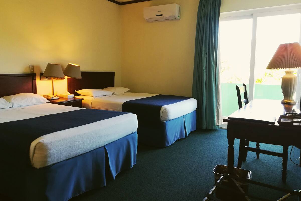 Ein Hotelzimmer mit zwei Betten, einem Schreibtisch, einem Stuhl, einer Lampe und einer Klimaanlage.