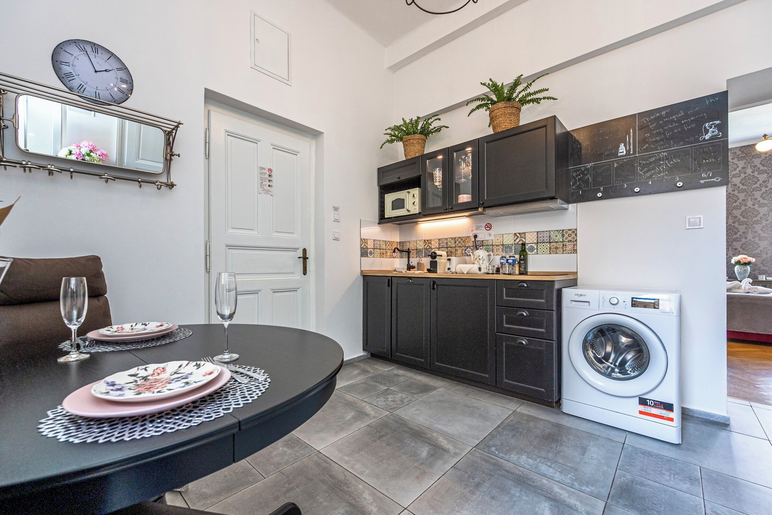 A compact kitchen with a microwave, oven, and washing machine. There is a dining table with plates and glasses.