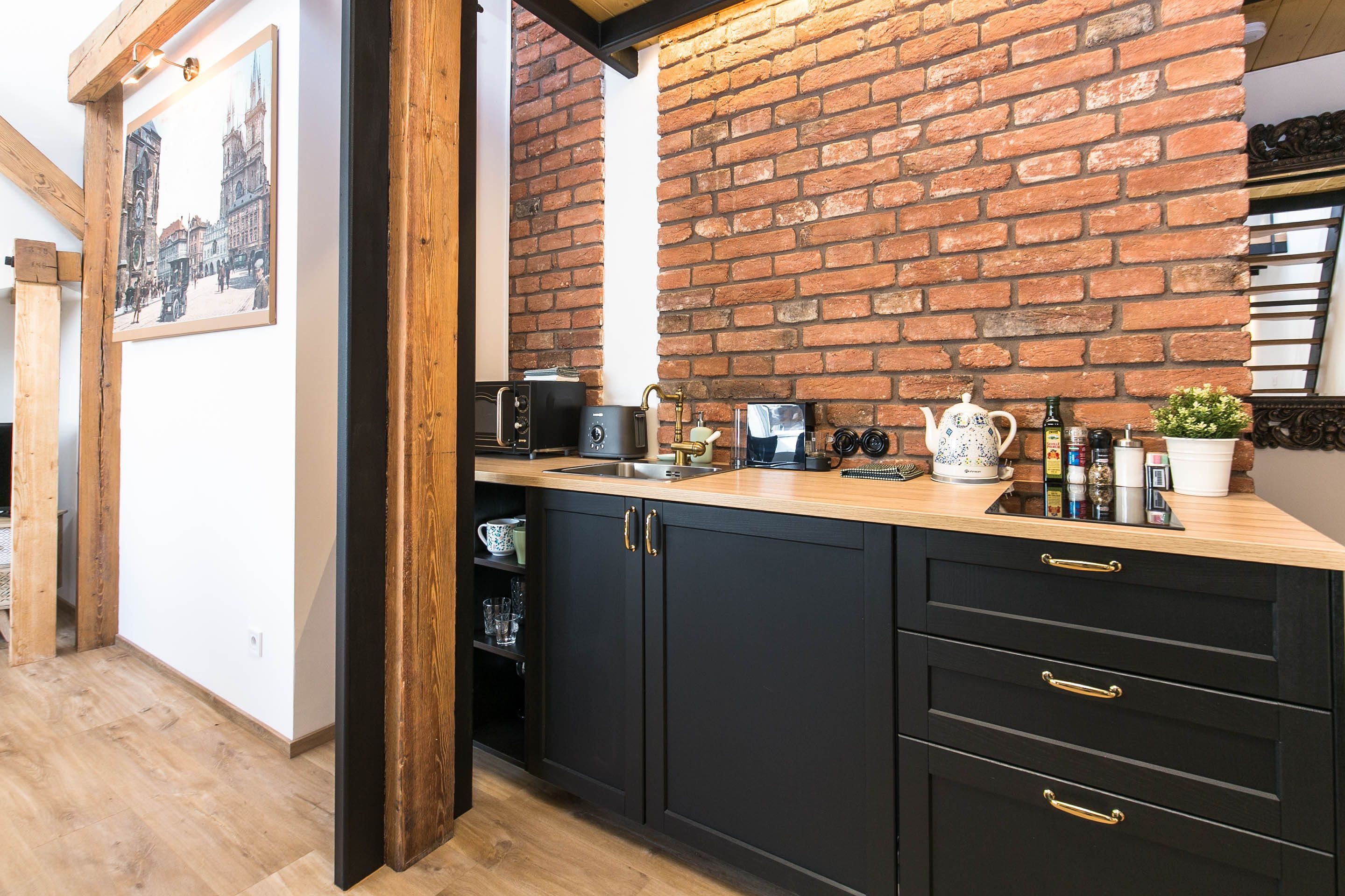 A kitchen with a brick wall, wooden beams, and black cabinets with gold handles.