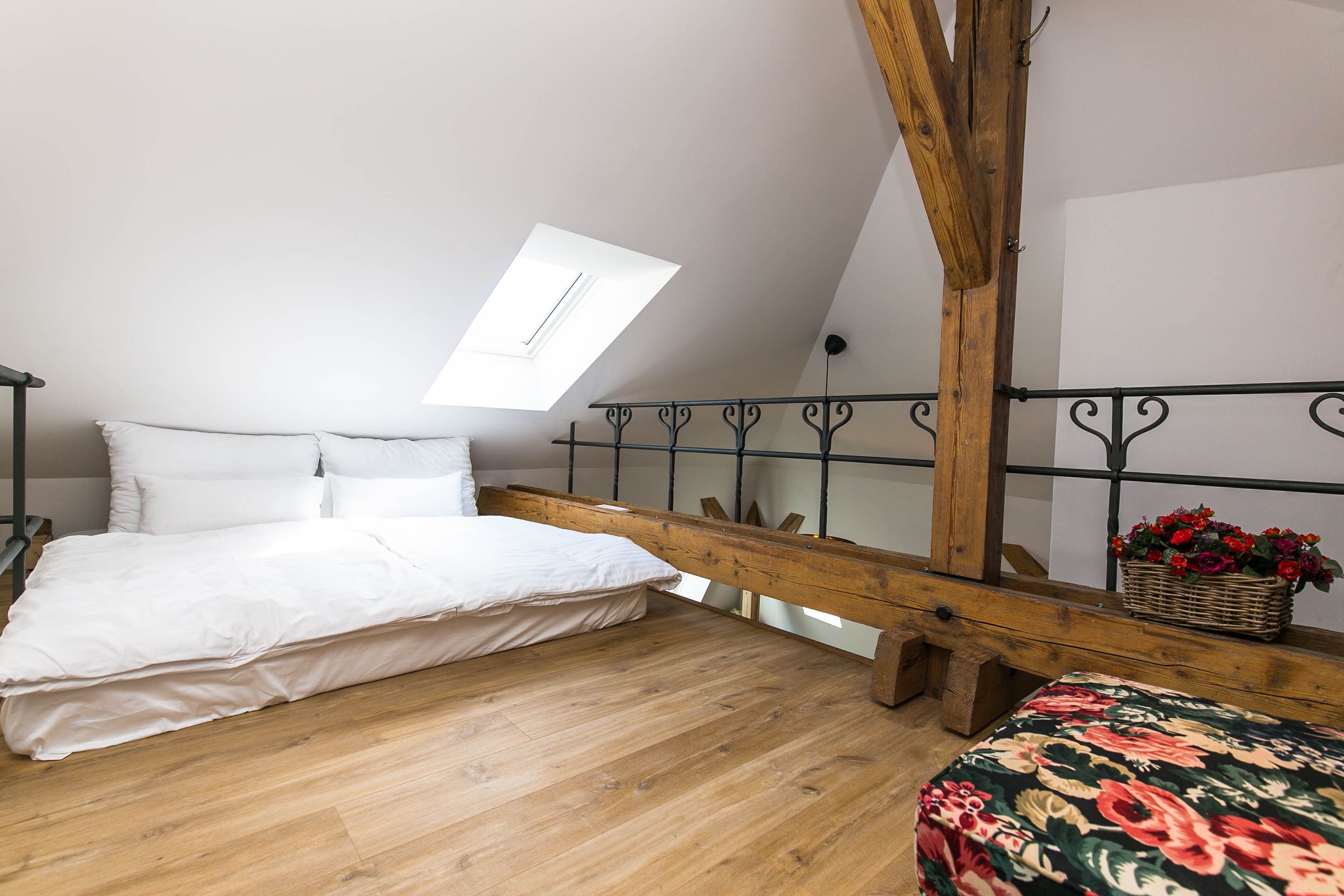 A bedroom with a wooden bed, a skylight, a balcony with a railing, and a wicker basket with flowers.