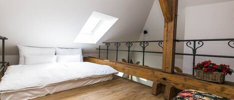 Un dormitorio con una cama de madera, tragaluz, balcón con barandilla y una cesta de mimbre con flores.