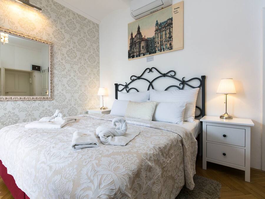 A neatly made bed with a patterned bedspread, a large mirror, a nightstand with a lamp, and a framed picture on the wall.