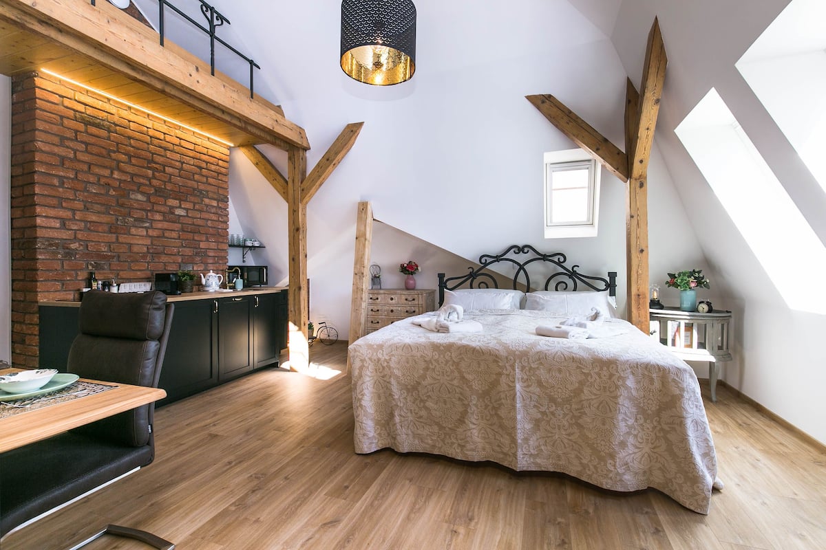 A bedroom with a large bed, wooden beams, a brick wall, and a skylight.