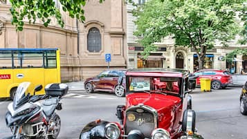 A vintage car, a yellow bus, and a motorcycle parked on a street with buildings in the background.