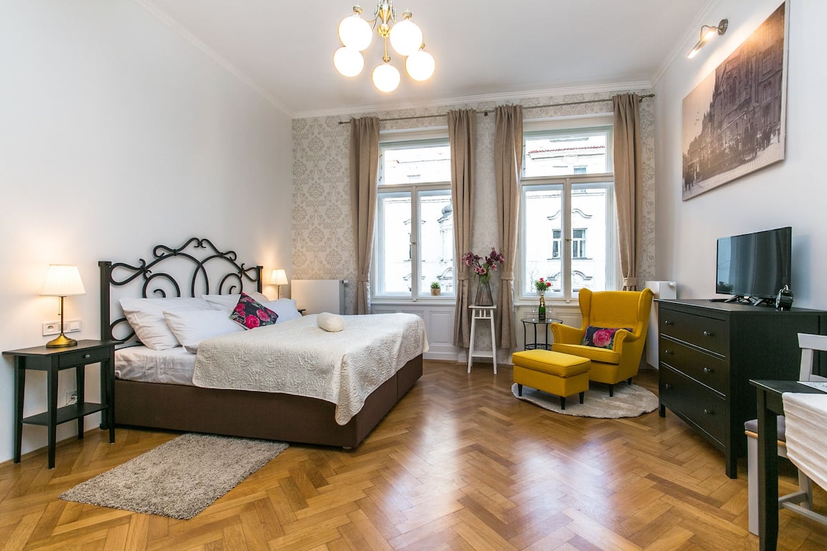 A bedroom with a bed, bedside tables, a chair, a dresser, a television, and a window with curtains.