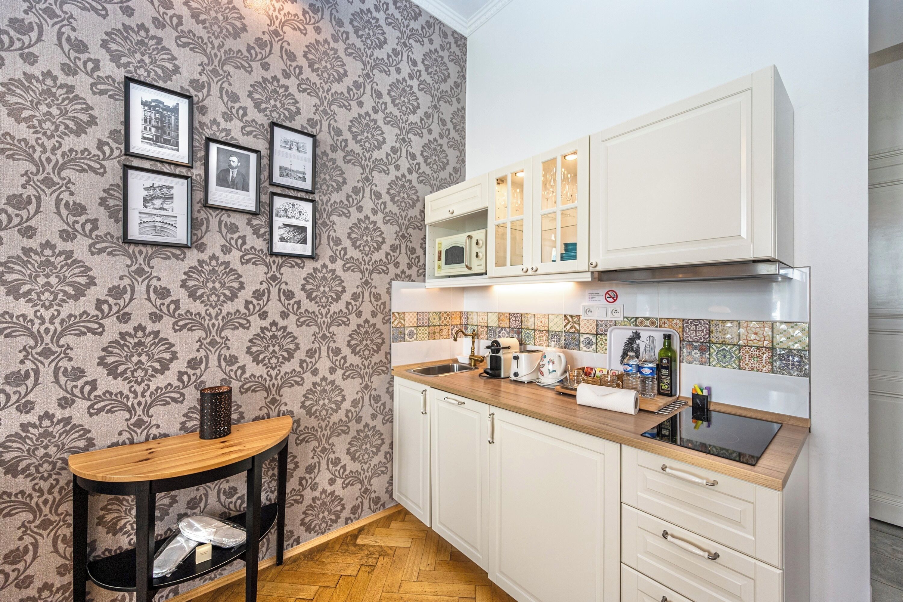 Una cocina con armarios blancos, encimera de madera y papel tapiz con estampado en espiga.