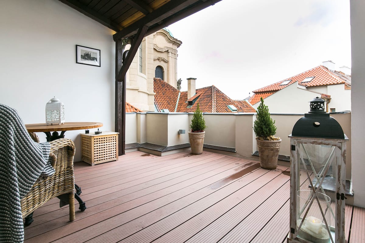 A wooden deck with wicker furniture, potted plants, and a lantern.
