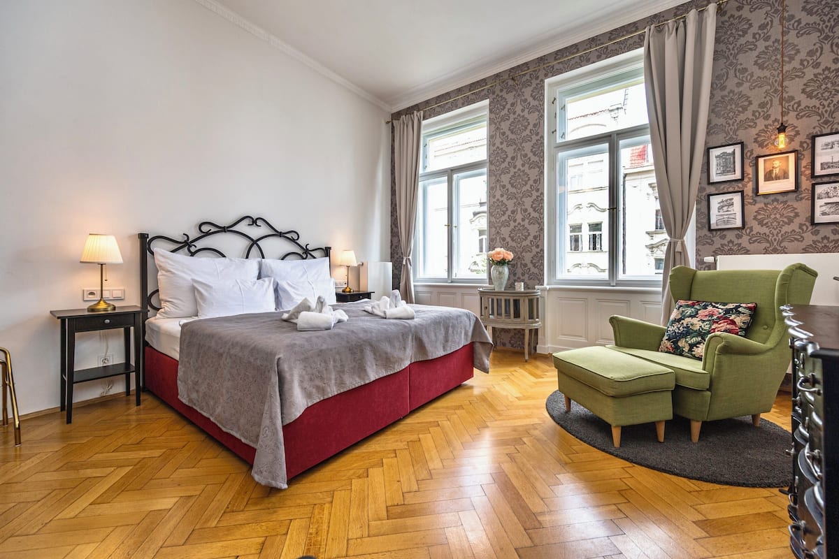 A neatly arranged bedroom with a bed, bedside tables, a chair, and a window with curtains.