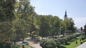 A park with a paved path, green lawns, and a church with a tall steeple. - Hotel Kralj Tomislav (Nova Gradiska)