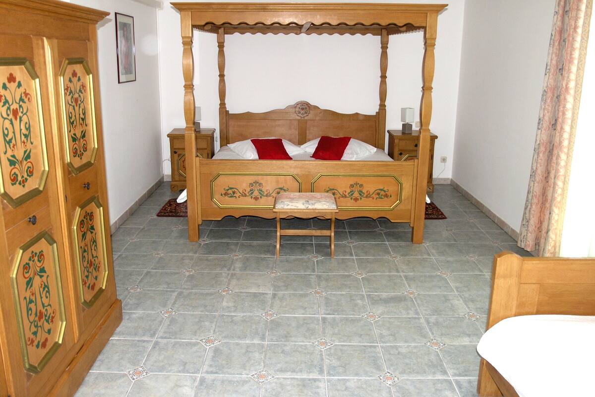 Ein Bett mit Himmelbett, ein hölzernes Kopfteil, zwei Nachttische und ein Beistelltisch.