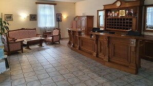 A hotel lobby with a sofa, chairs, a wooden reception desk, and a tiled floor. - Hotel Kralj Tomislav (Nova Gradiska)