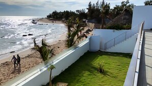 A balcony with a view of the beach, a grassy area with plants, and a white wall.