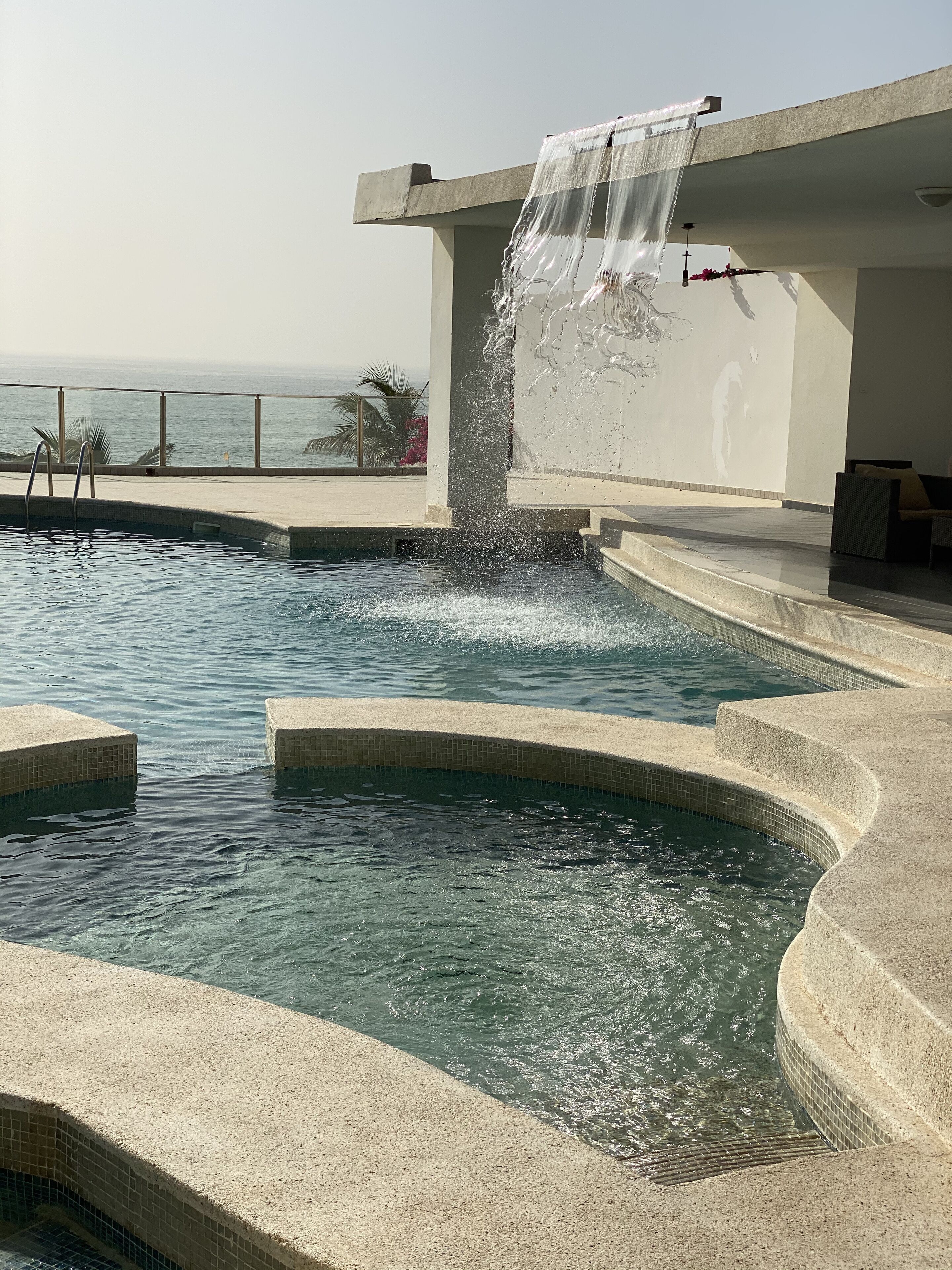 Ein Pool mit Wasserspiel, Meerblick und eine Lounge mit einer Couch.