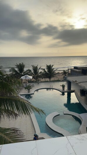 A pool area with a view of the ocean, palm trees, and a cloudy sky. - Villa Somone Pied Dans L'eau (La Somone)