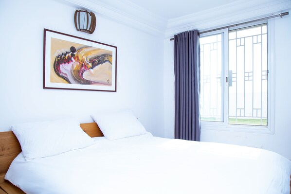 Un dormitorio con cama, un cuadro, una ventana con cortinas y vistas al exterior.
