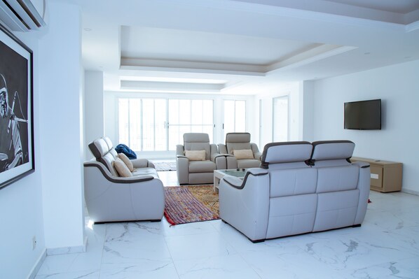 A modern living room with a sofa, chairs, a coffee table, and a TV mounted on the wall.