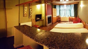 A hotel room with a granite countertop, a television, a fireplace, a bed, and a window with curtains.