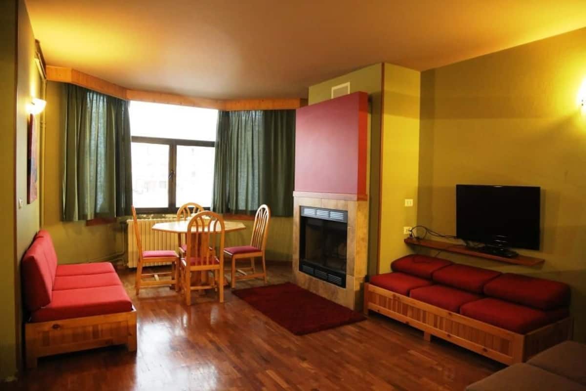 Una sala de estar con chimenea, televisor y comedor con sillas y mesa.