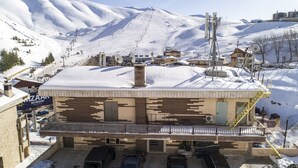 A building with a ski resort sign, a parking area with several cars, and a snowy mountain backdrop.