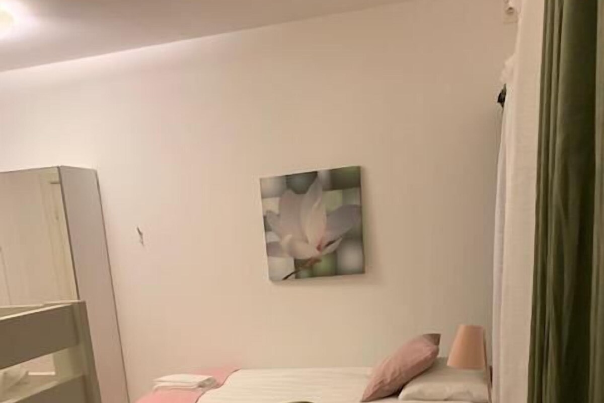 Een kleine, verzorgde kamer met een bed, een stoel, een tafel en een schilderij aan de muur.