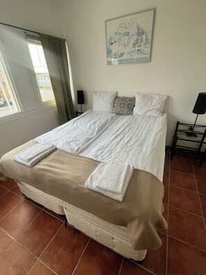 A hotel room with a large bed, a painting on the wall, a window with curtains, and a tiled floor. - Mälarö Hotell (Ekerö)