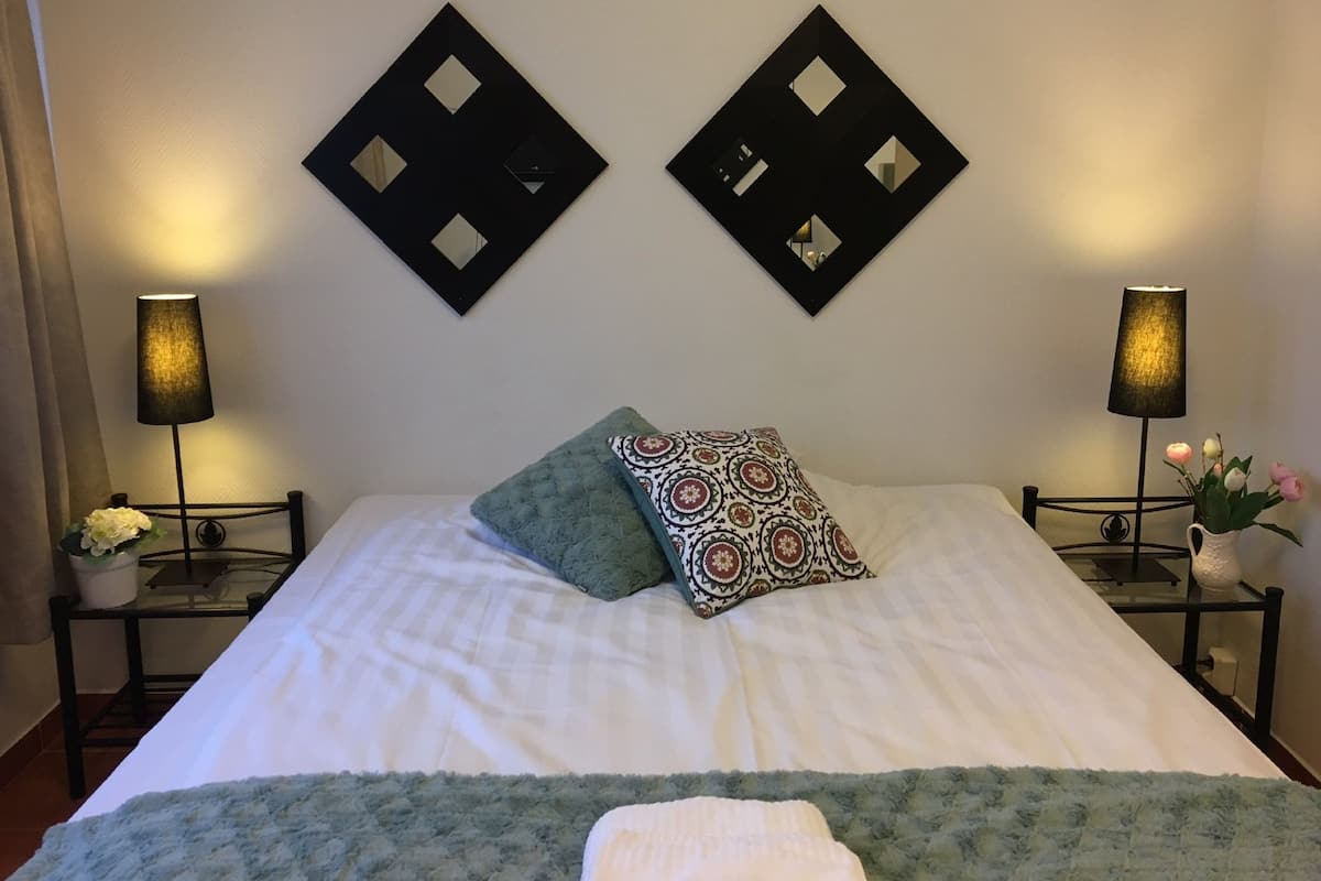Una cama bien hecha con dos almohadas, dos mesitas de noche con lámparas y un adorno en la pared.