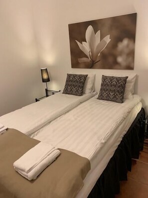 A double bed with two pillows, a bedside lamp, and a wall-mounted picture of a flower. - Mälarö Hotell (Ekerö)