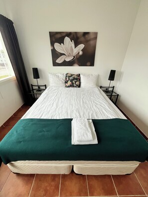 A neatly made bed with a green bedspread and a white towel folded on it. - Mälarö Hotell (Ekerö)
