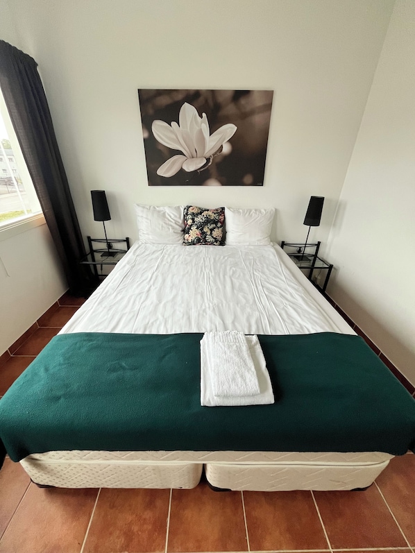 Una cama bien hecha con una colcha verde y una toalla blanca doblada encima.