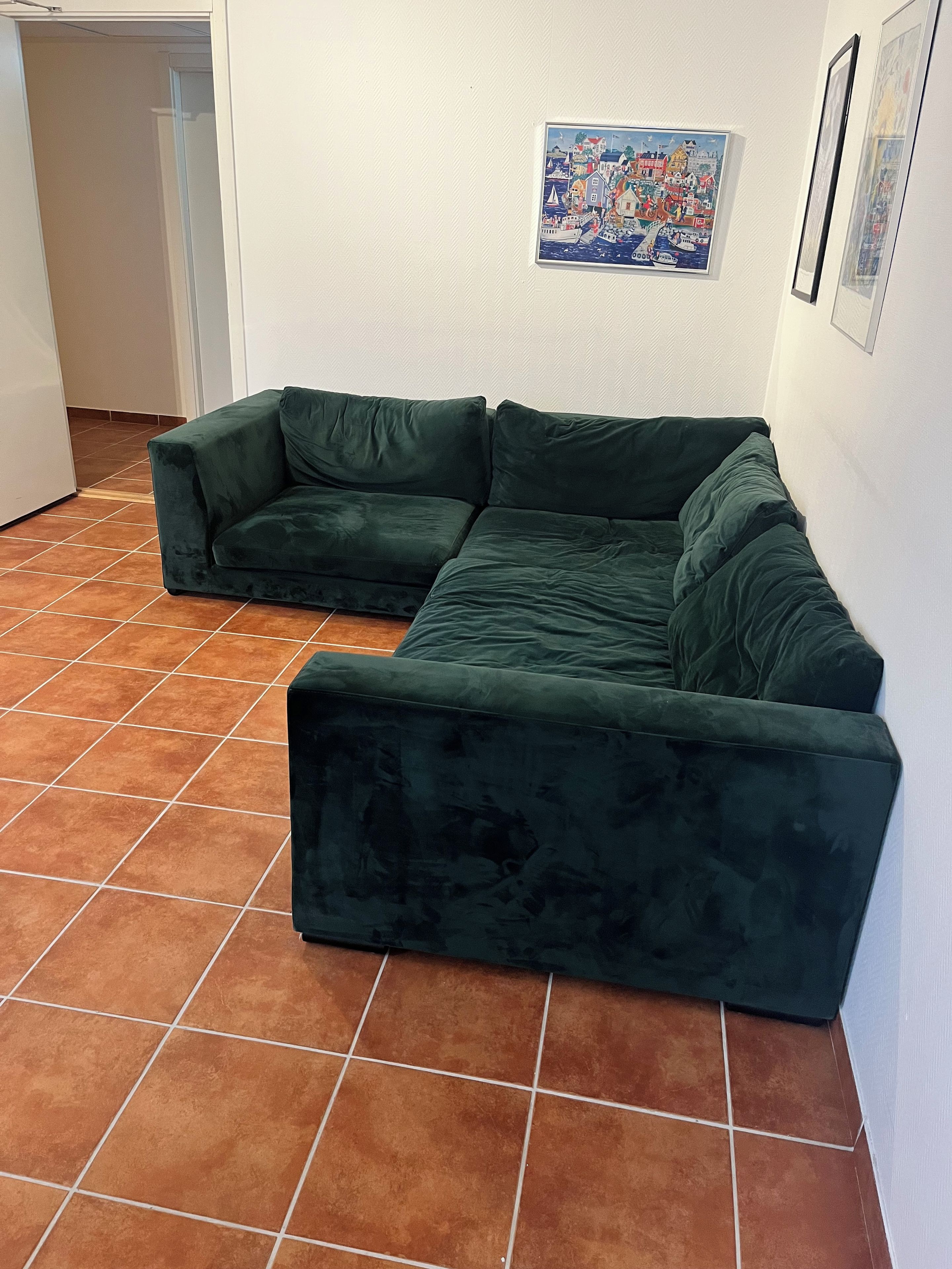 A green sectional sofa in a room with a tiled floor and a framed painting on the wall.