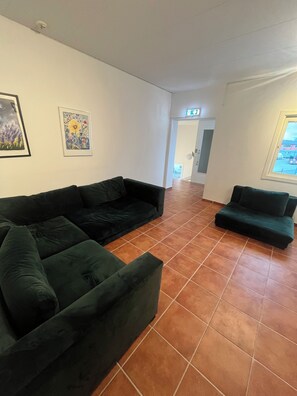 A spacious living area with two dark green sofas, a tiled floor, and two framed artworks on the walls. - Mälarö Hotell (Ekerö)