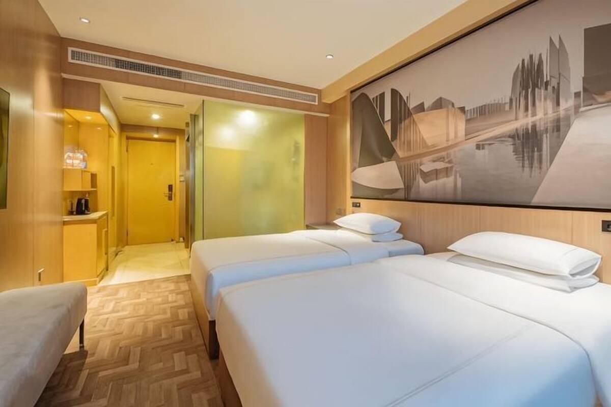 Een hotelkamer met twee bedden, een bureau, een stoel en een groot stadslandschap op de muur.