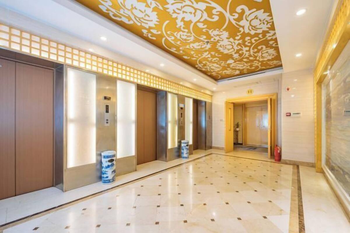 Een hotellobby met een marmeren vloer, een decoratief plafond en een rij liften.