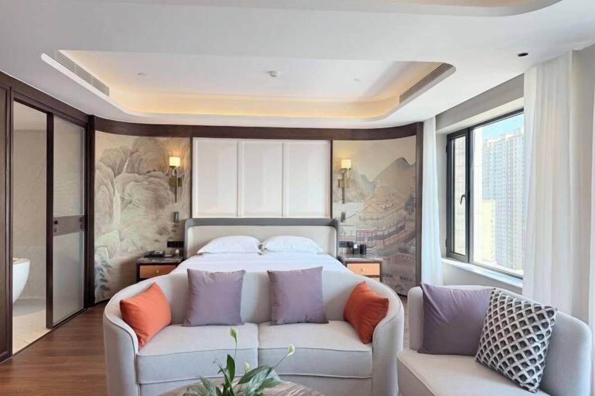Een moderne hotelkamer met een groot bed, twee nachtkastjes, een bank en een groot raam.