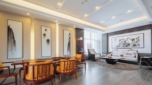 Una sala de estar moderna con comedor, que presenta muebles de madera, obras de arte en las paredes y un gran ventanal que proporciona luz natural.