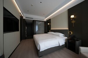 Una habitación de hotel moderna con una cama grande, mesitas de noche, un televisor y un vestidor.