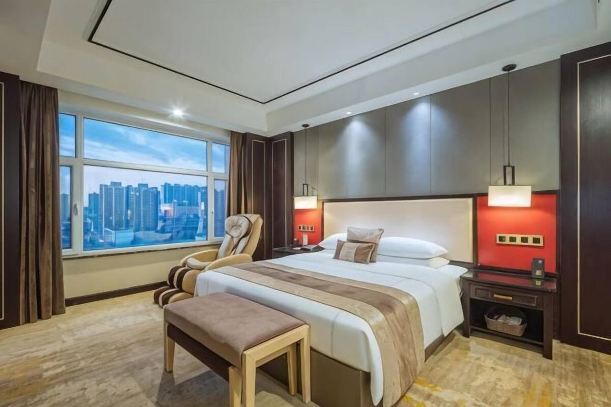 Een moderne hotelkamer met een groot bed, een zithoek, een nachtkastje en uitzicht op de stad.
