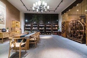 A spacious room with a long wooden table and chairs, a chandelier, and bookshelves filled with books. - Luban Hotel (Tengzhou)
