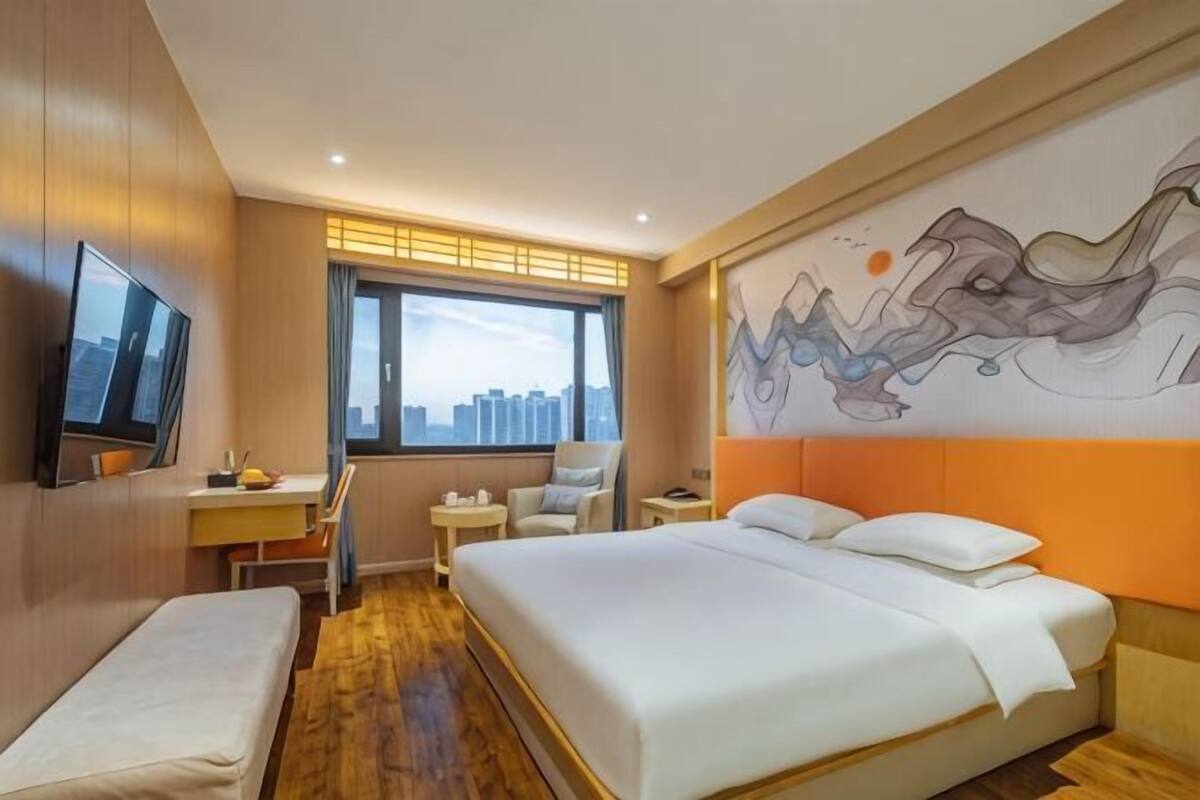 Een hotelkamer met een bed, een bureau, een stoel, een televisie en uitzicht op de stad.