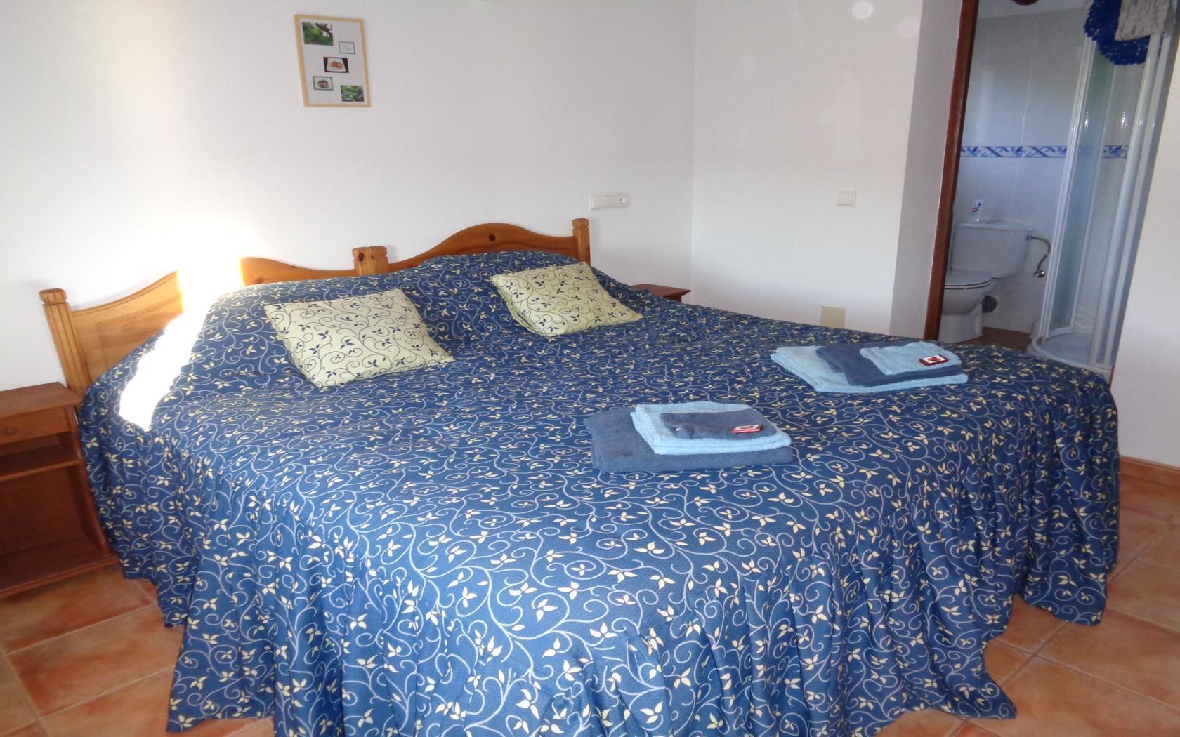 Ein Schlafzimmer mit Bett, zwei Kissen, einem Holzkopfende und einem durchgegangenen Türrahmen sichtbaren Badezimmer.