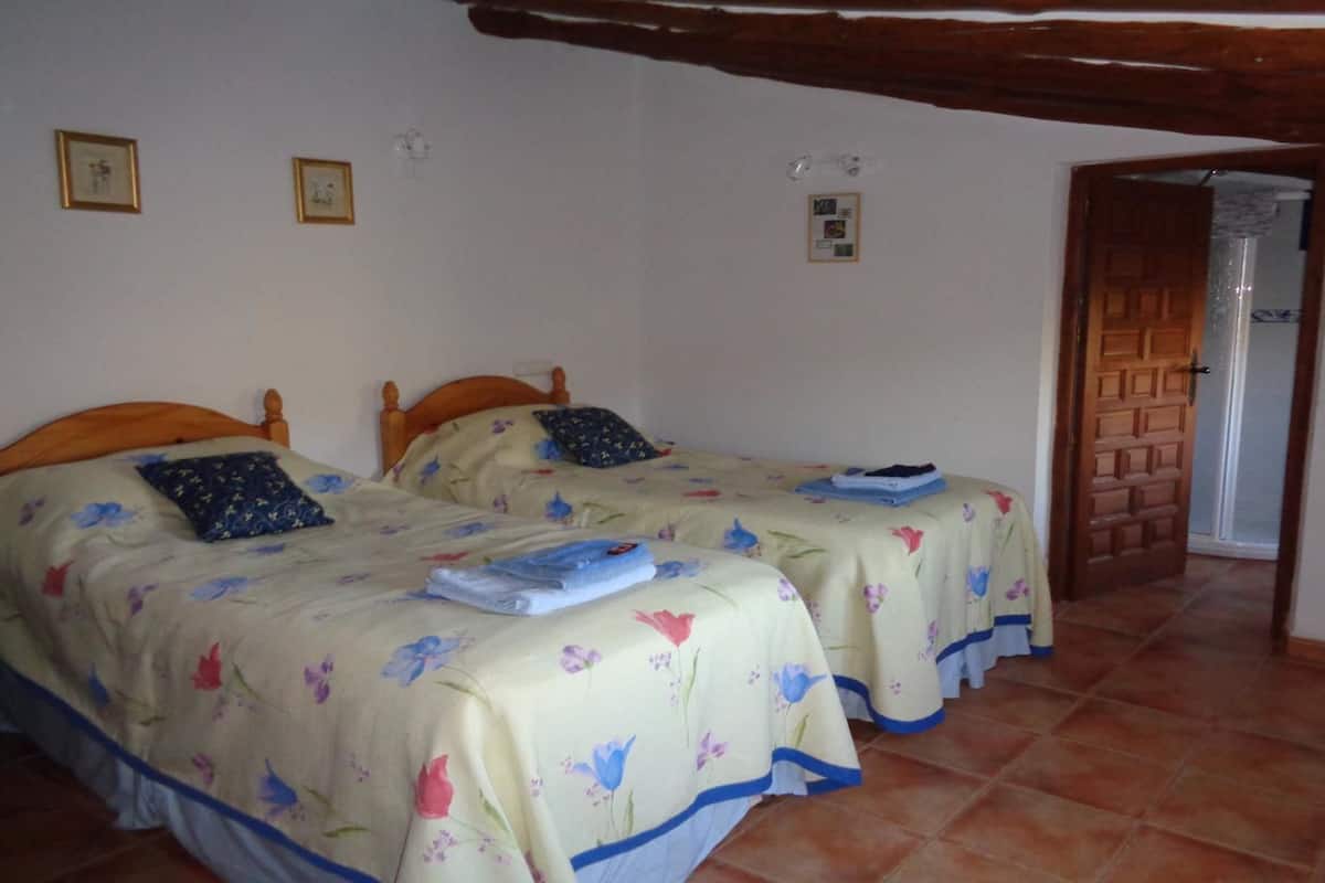 Une chambre dotée de deux lits, chacun agrémenté de draps et d’oreillers à motifs floraux, de têtes de lit en bois et d’un sol carrelé.