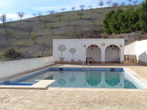 Une piscine avec une terrasse carrelée, un espace salon couvert et une vue sur une colline en arrière-plan.