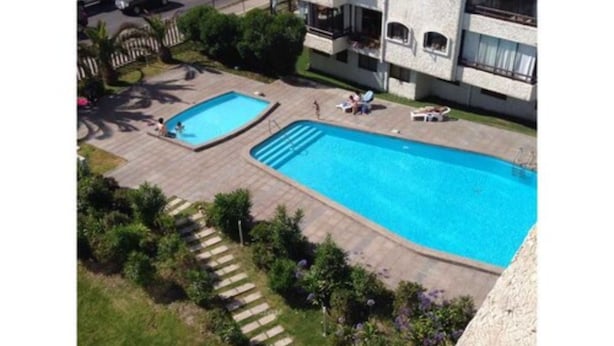 Une grande piscine rectangulaire, avec une piscine plus petite attenante, le tout entouré d’une terrasse dallée et de marches menant à une zone herbeuse.