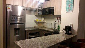 A compact kitchen with a stainless steel refrigerator, a microwave, and a coffee maker on the countertop. - Departamento Gran Marina (La Serena)