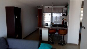 A compact living space with a kitchenette, a sofa, and a dining area with stools. - Departamento Gran Marina (La Serena)