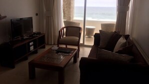 A living room with a television, a coffee table, a sofa, and a chair. There is a large window with a view of the ocean. - Fragata 802 (Coquimbo)