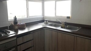 A kitchen with wooden cabinets, a stainless steel sink, and a window providing natural light. - Piscina Cristalina Coral (La Serena)