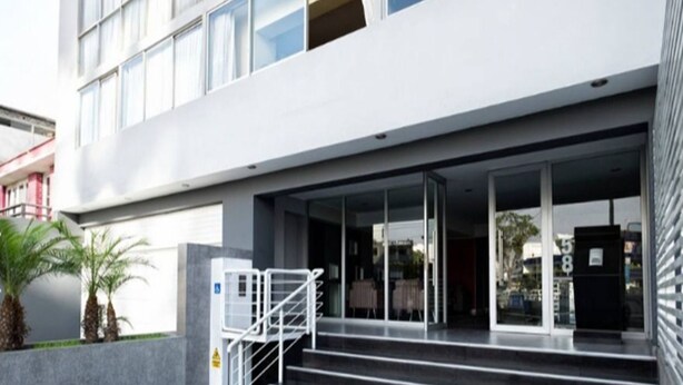 Un bâtiment moderne avec un escalier menant à une entrée en verre, des places assises à l’extérieur et une poubelle.