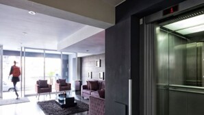 Un hall d’entrée moderne avec un ascenseur en verre, un canapé et une table basse.